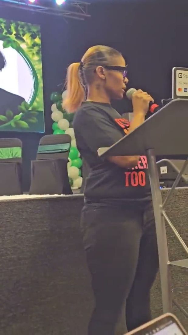 Dr. Gee presenting on stage with a microphone at a lectern