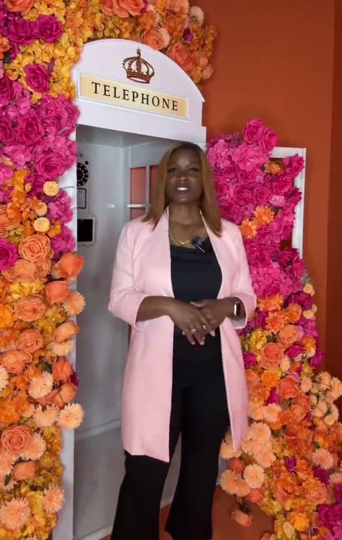 Dr. Gee in a pink blazer beside a telephone booth framed in orange and pink flowers